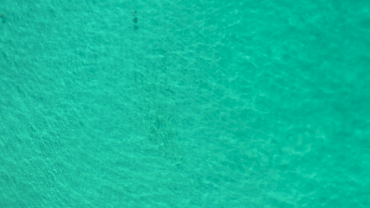 Pale turquoise water in Los Cabos shows shifting light patterns and a darker vertical mark near the lower edge, with no visible people.