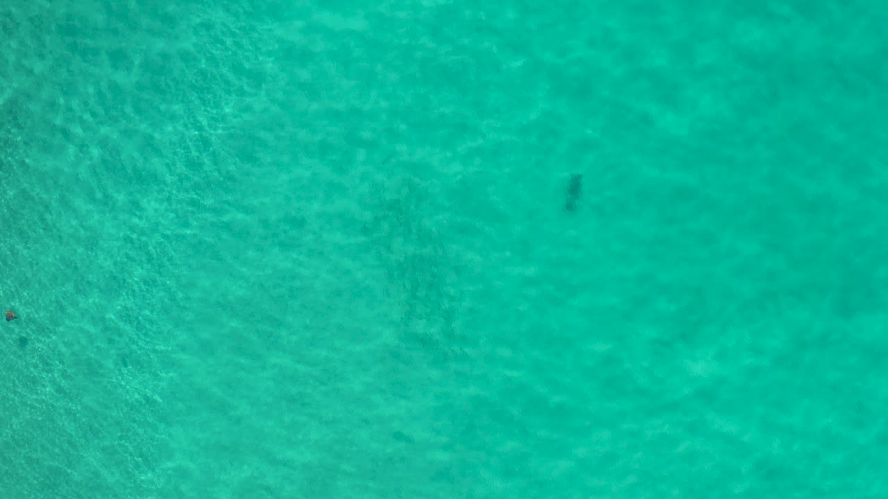 Turquoise ocean water seen from above with faint sandy texture below.