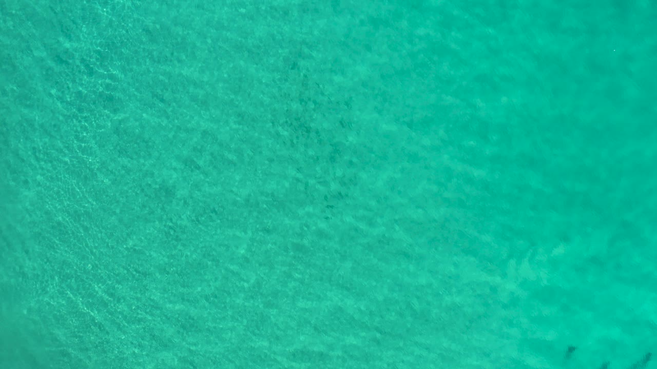 Overhead view of turquoise-green seawater in Los Cabos, Mexico, with faint ripples and no visible people.