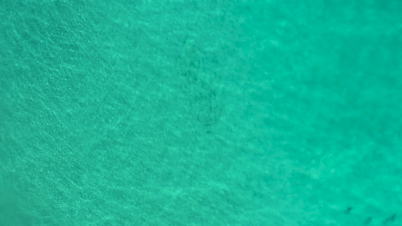 Turquoise sea surface in Los Cabos, Mexico, shows faint darker underwater patches near the edge of the frame and no visible people.