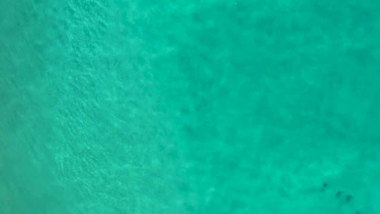 Aerial frame of aqua ocean water in Los Cabos, Mexico, with soft wave patterning across the upper left and no visible people.