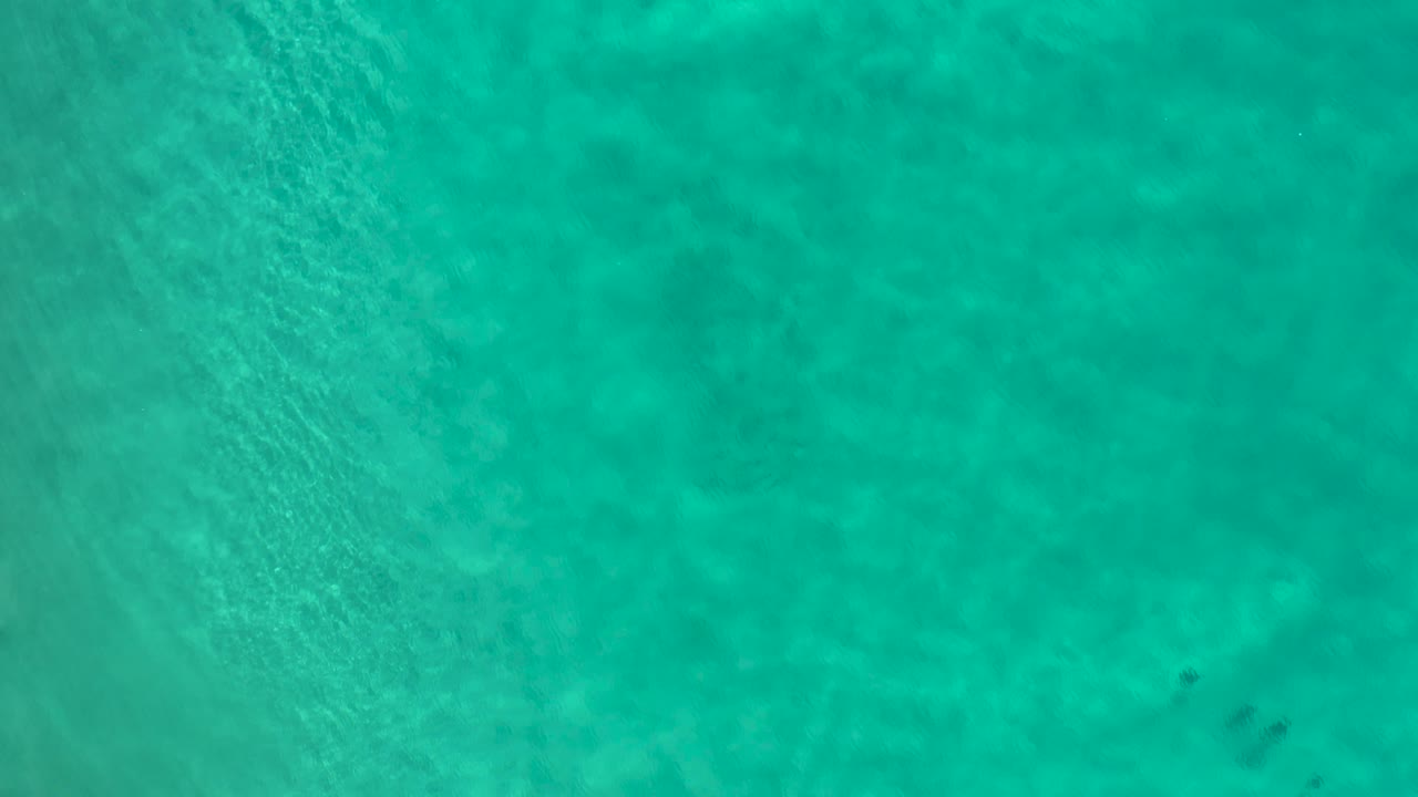 Overhead Los Cabos water frame with teal color, subtle bottom variation, small darker underwater patches near the right side, and no visible people.