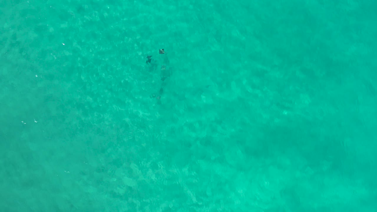 Overhead view of turquoise ocean water in Los Cabos, Mexico, with faint darker patches near the upper left and no visible people.