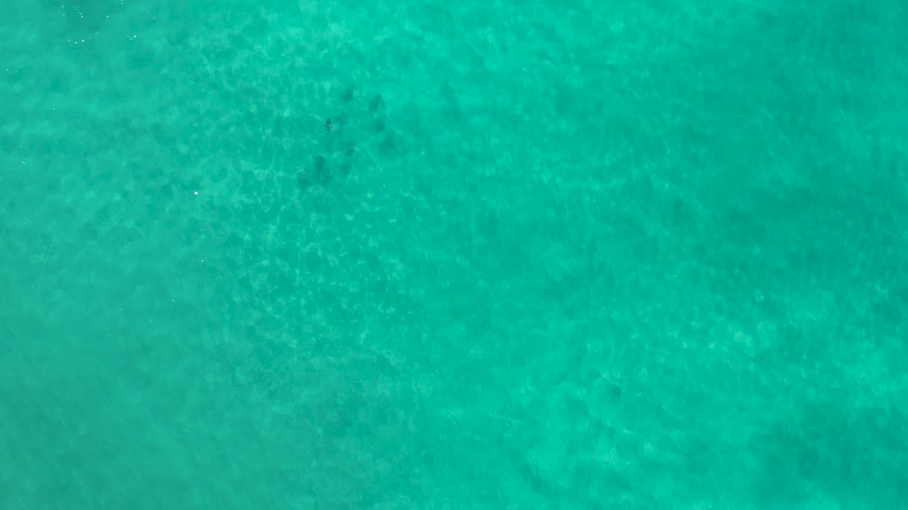 Overhead view of turquoise Los Cabos sea water with mottled sand visible below and no visible people.