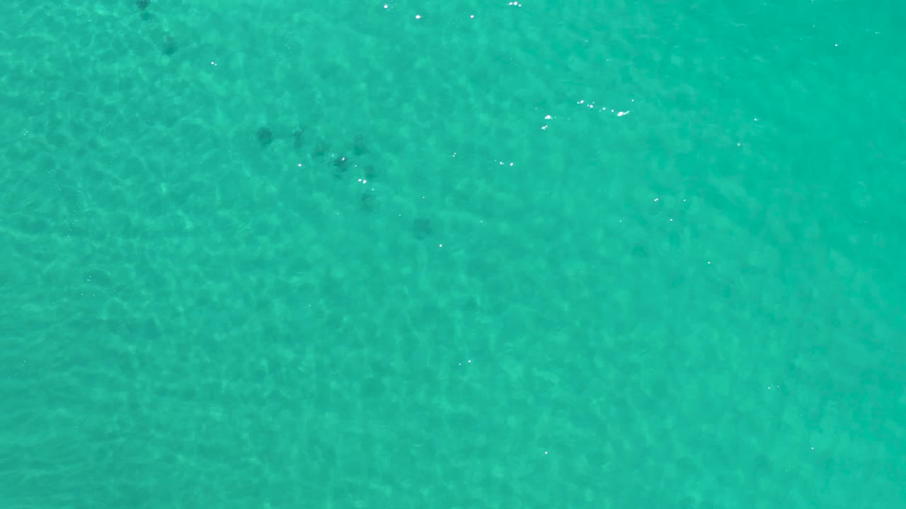Straight-down aerial frame of blue-green Los Cabos ocean water with fine surface texture, a few bright reflections, and no visible people.