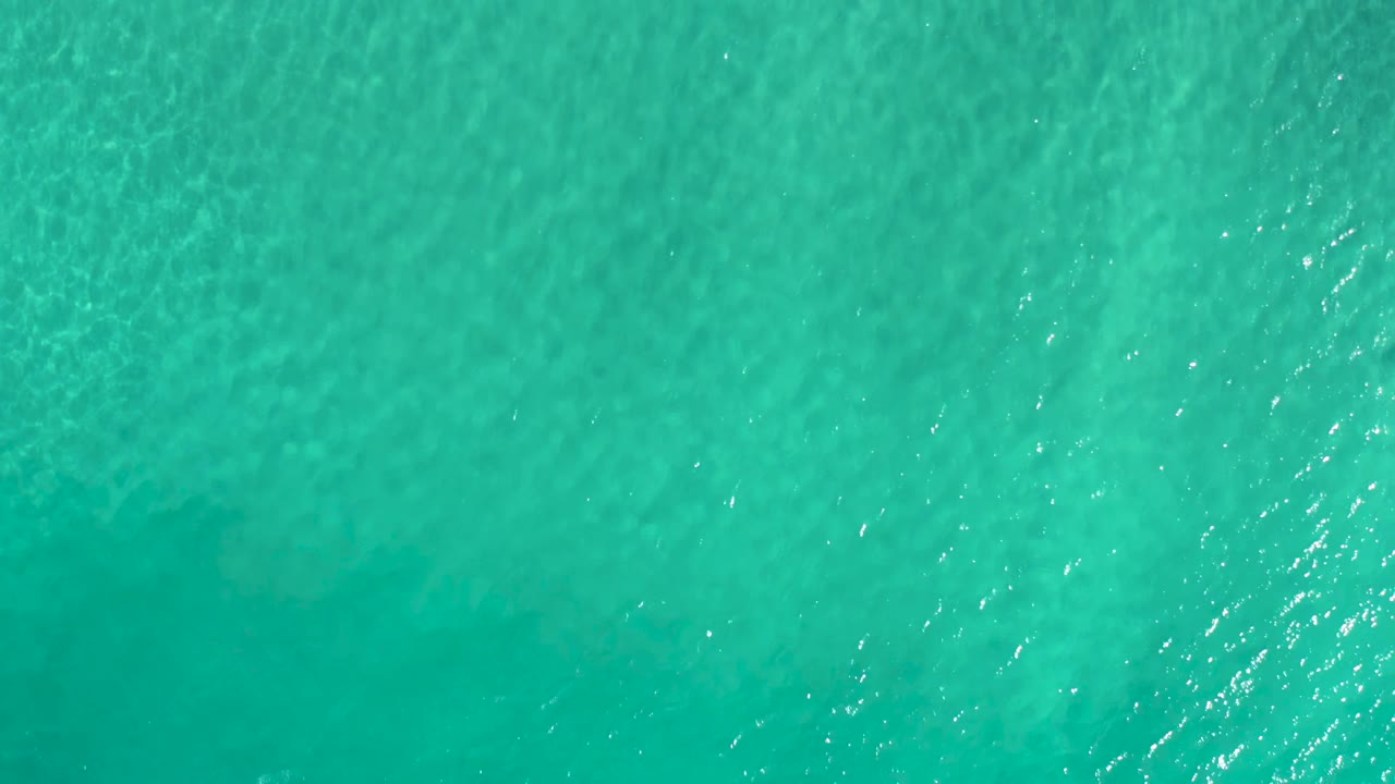 Aerial frame of clear green ocean in Los Cabos, Mexico, with subtle shallow-water patterns and no visible people.