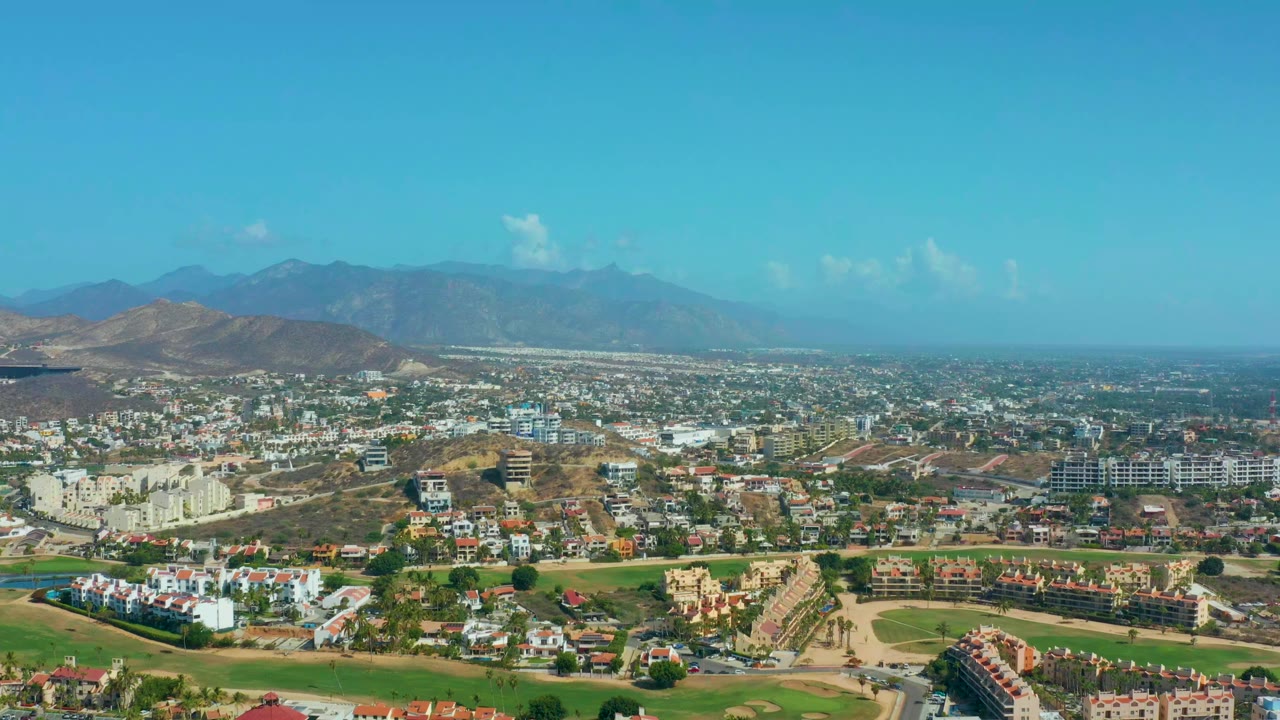 Aerial view across low-rise buildings, green grounds, and mountains in Los Cabos.