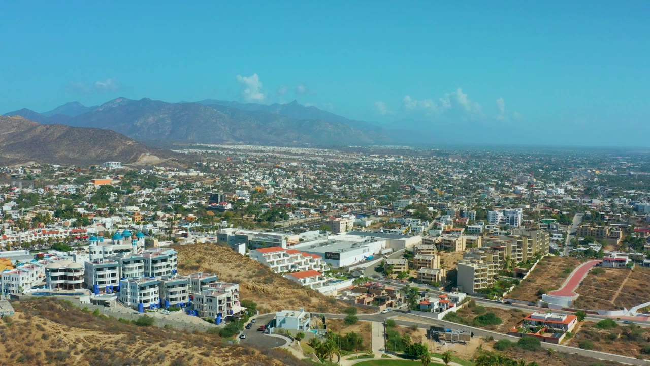 Third frame shows Los Cabos neighborhoods and commercial-looking buildings spread below a mountain horizon, with a bright blue sky and no visible people.