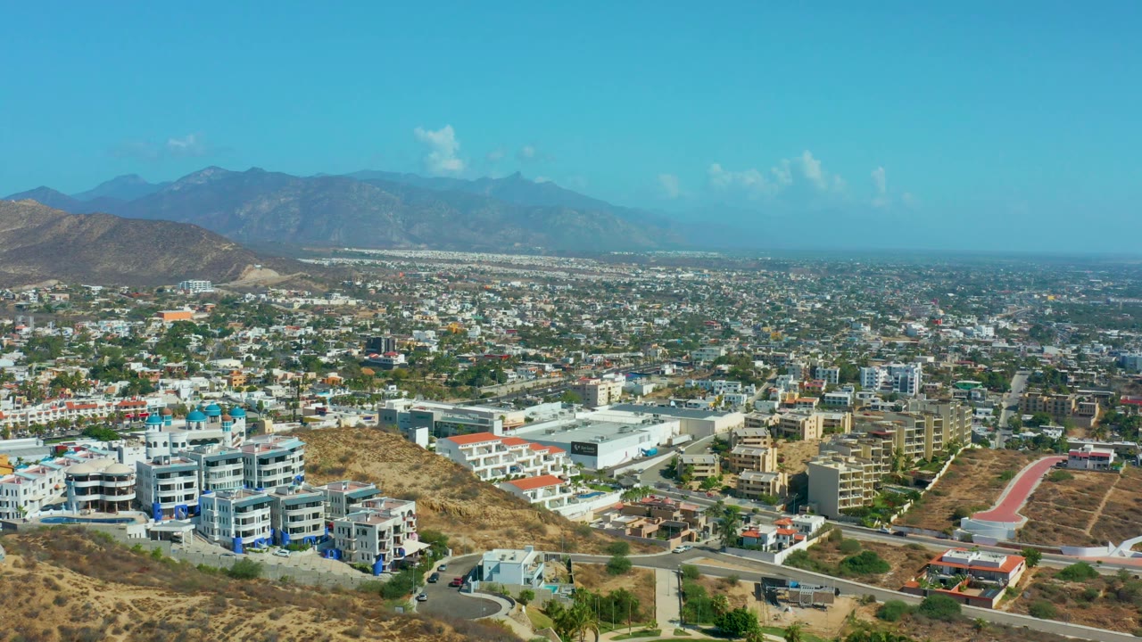 Modern buildings and roads below a wide sky and distant mountains.