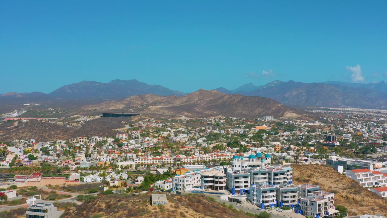 Los Cabos hillside community seen from above with buildings, roads, hills, and mountains.