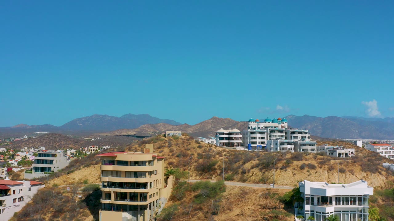 Hillside neighborhood with tan condo building in front and mountains behind