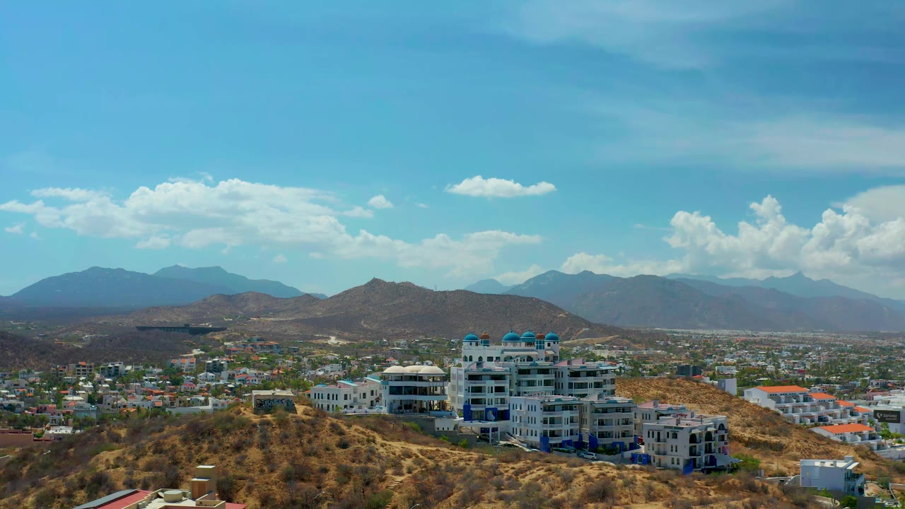 Hillside buildings overlook a low city with mountain ridges in the distance.