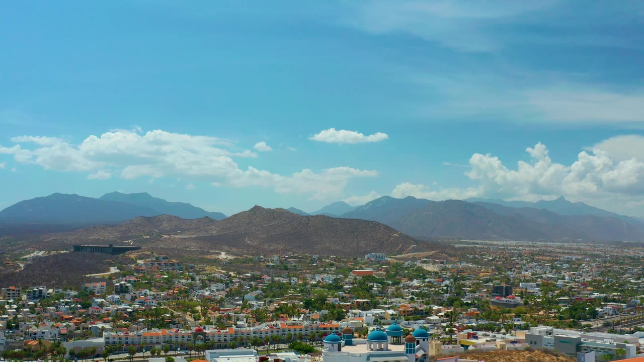 Aerial view across rooftops toward hills and a mountain skyline in Los Cabos.