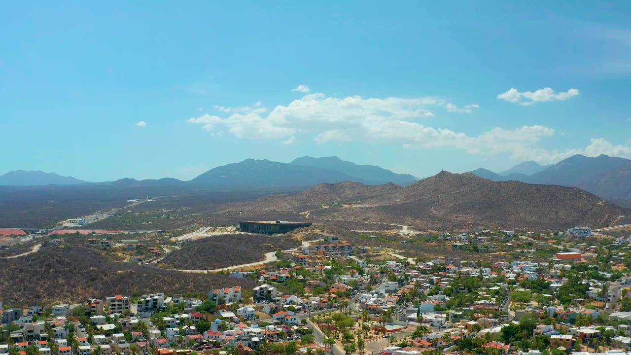 Suburban neighborhood with roads, low hills, and mountains under blue sky.