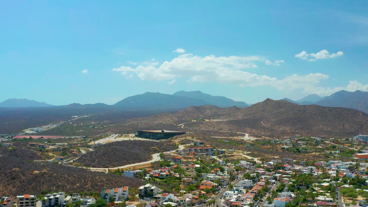 Aerial city edge with roads, hillside terrain, and mountain horizon.