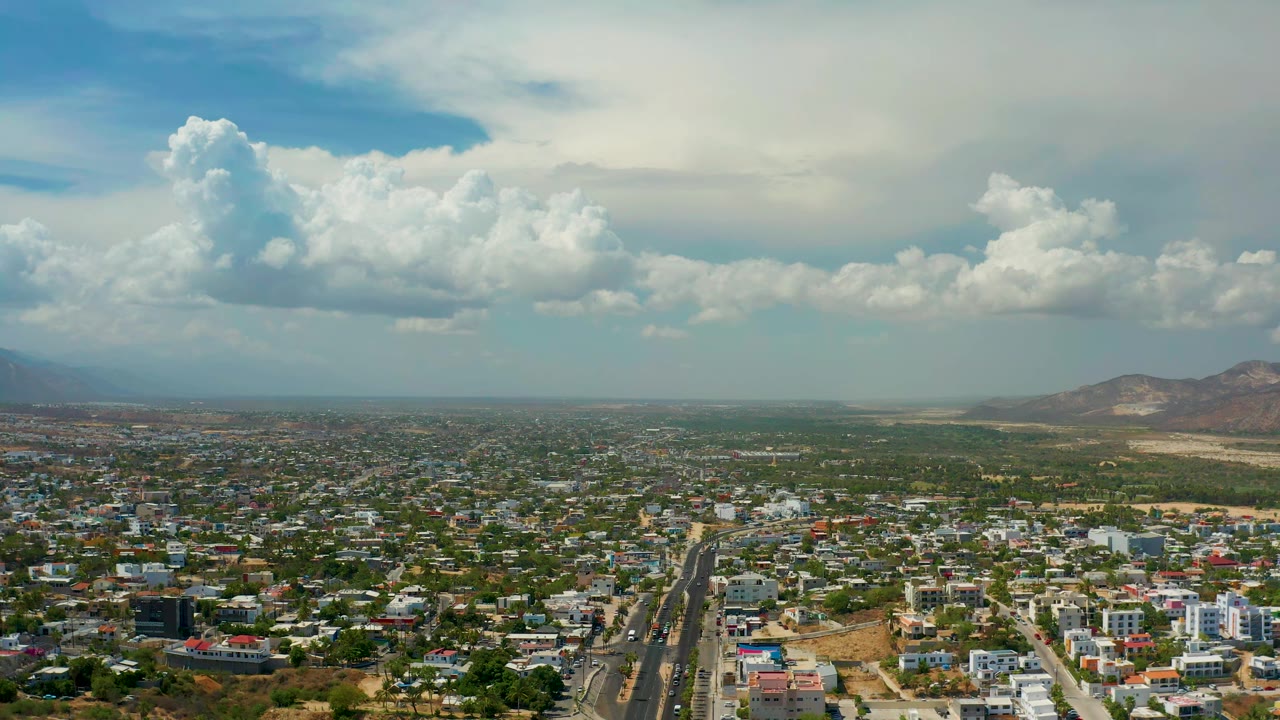 Aerial view across Los Cabos homes and streets, with the central road pulling toward the horizon and no visible people in the frame.