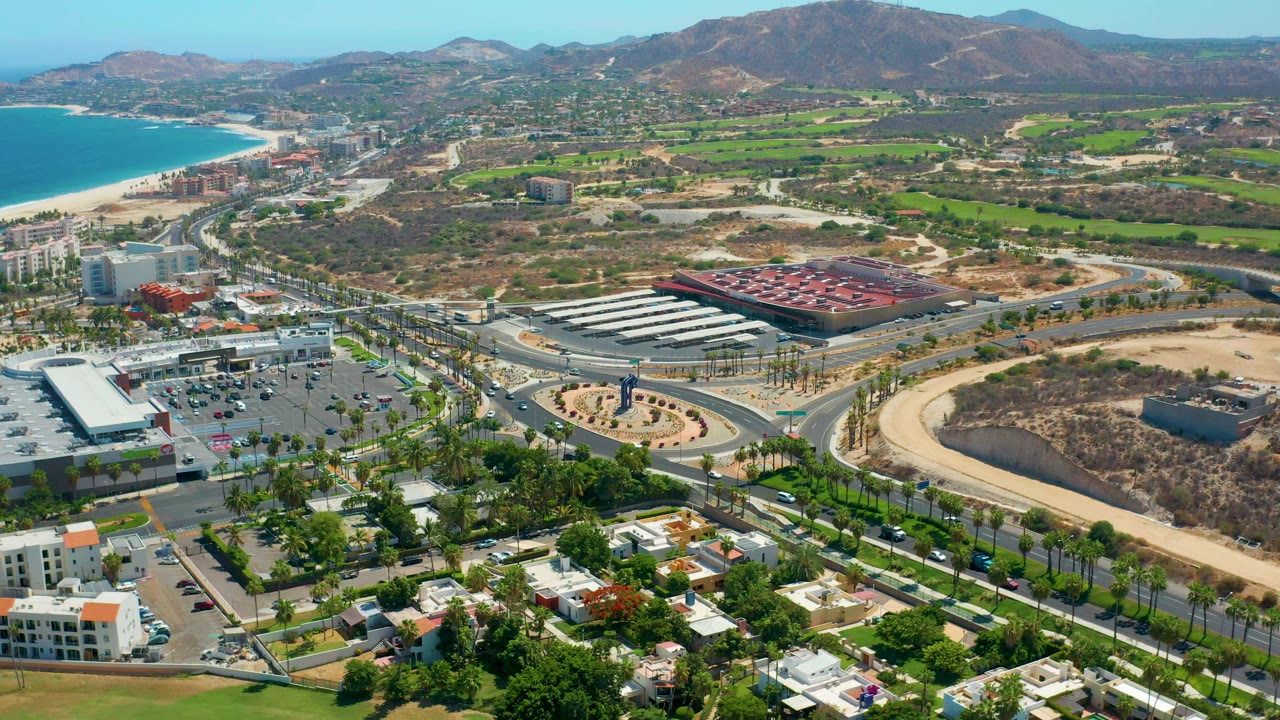 Wide drone-like view of highway, shopping area, homes, coastline, and hills.