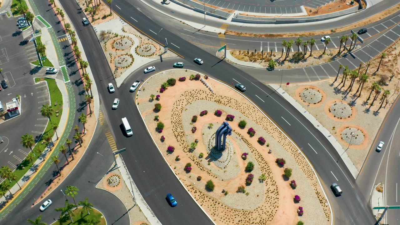Cars travel along intersecting roads beside palm-lined sidewalks.