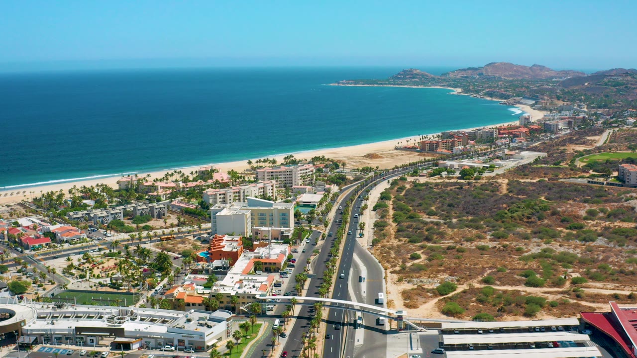 Aerial view of coastline, beach, town buildings, road, and hills.