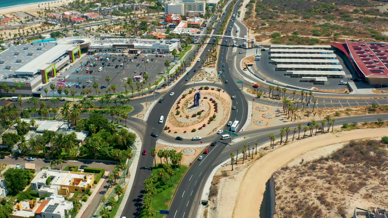 Third frame shows the Los Cabos roundabout, divided roads with small vehicles, palm rows, a parking lot beside large commercial buildings, dry open ground, and no visible people.