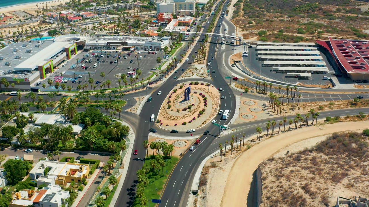 Aerial view of roundabout traffic, palm landscaping, commercial buildings, homes, and open lots.