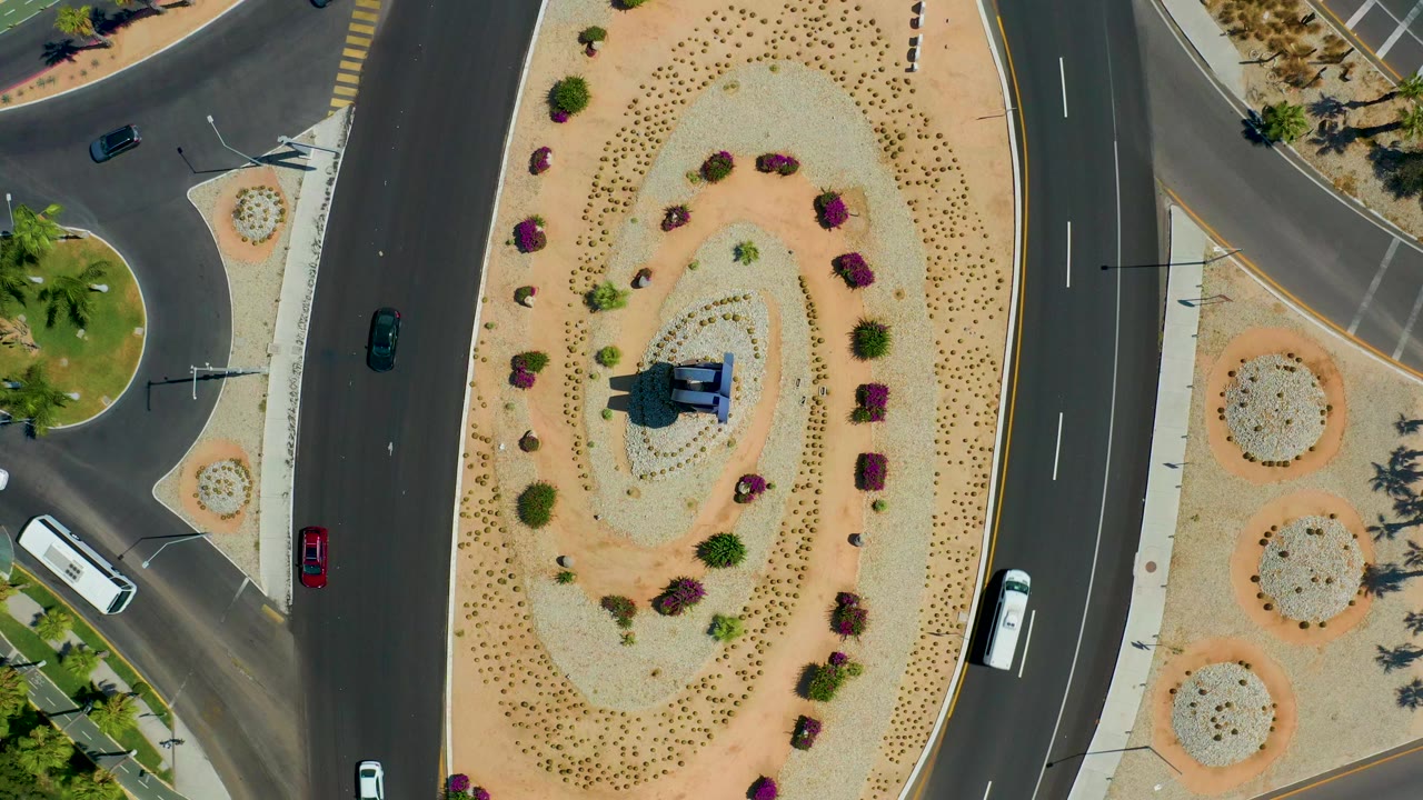 Overhead road curve around a desert landscaped median with cars and a white bus.