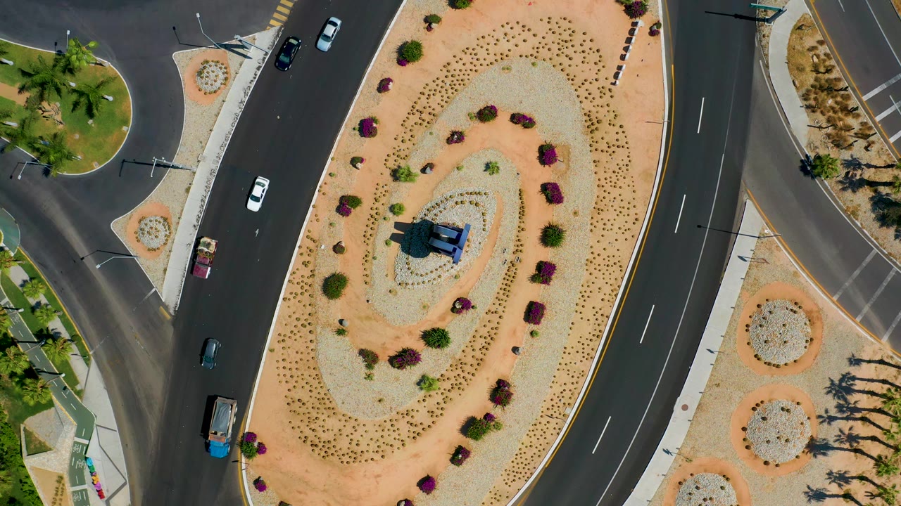 Cars move along curved streets beside a sandy median