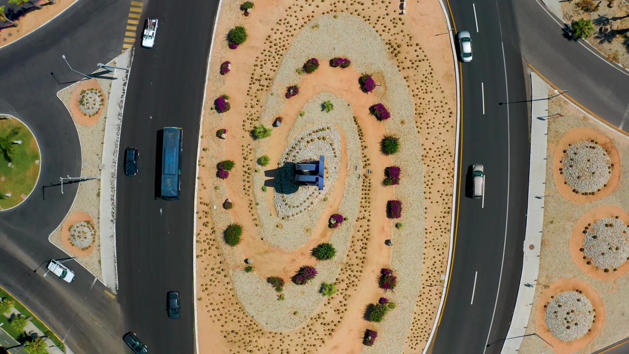 Traffic passes a landscaped roundabout island seen from directly above.