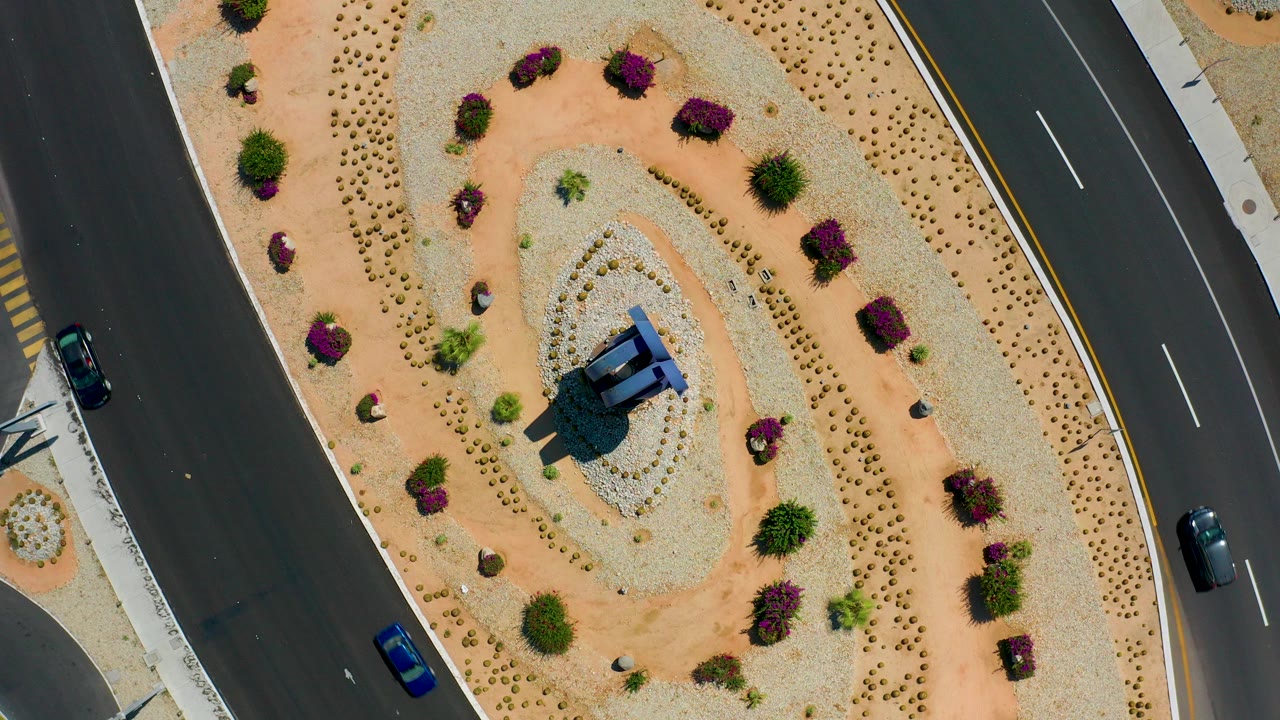 Overhead view of a landscaped roundabout beside dark roads with cars nearby.