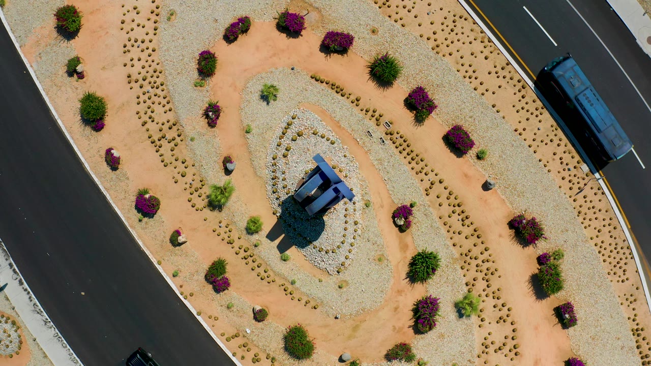 Top-down Los Cabos, Mexico frame showing the bus farther along the right lane, the planted gravel median filling most of frame, and no visible people.
