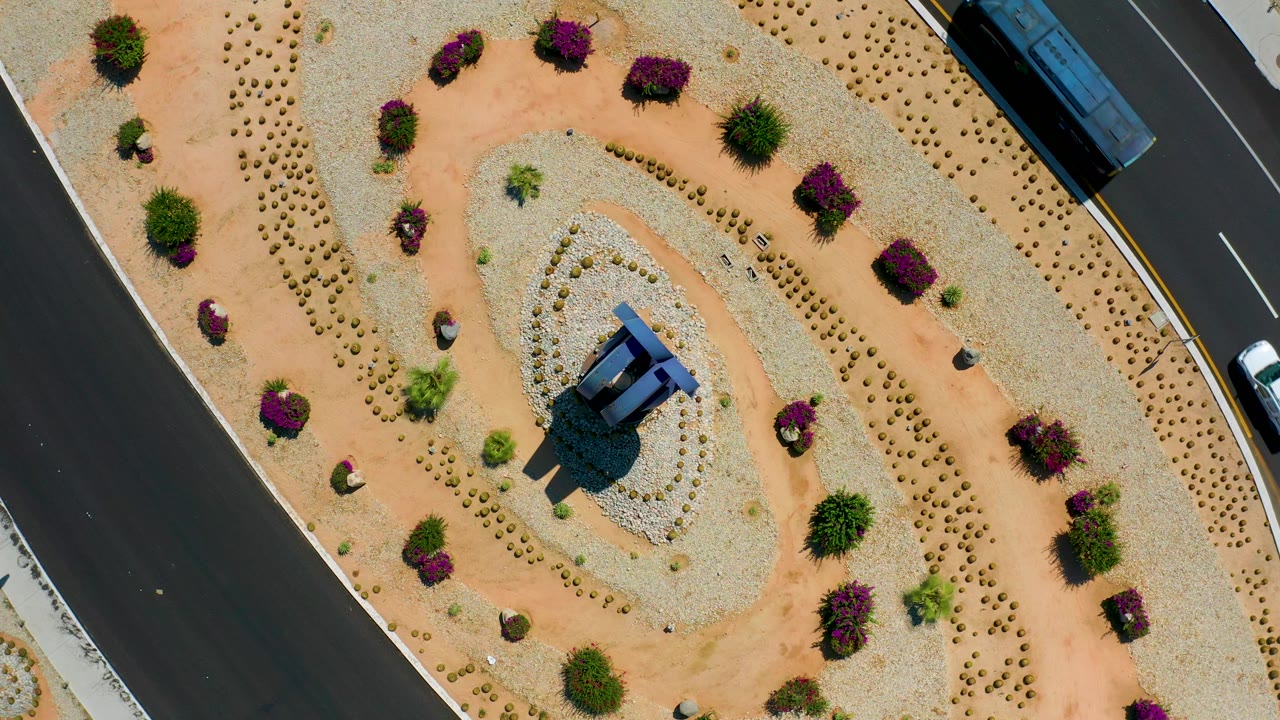 Aerial Los Cabos, Mexico frame with the bus partly near the upper road edge, the landscaped median below it, and no visible people.