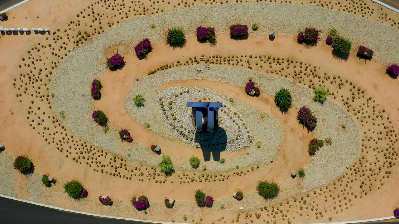 Aerial view of looping gravel beds, desert shrubs, and a centered blue shade structure.