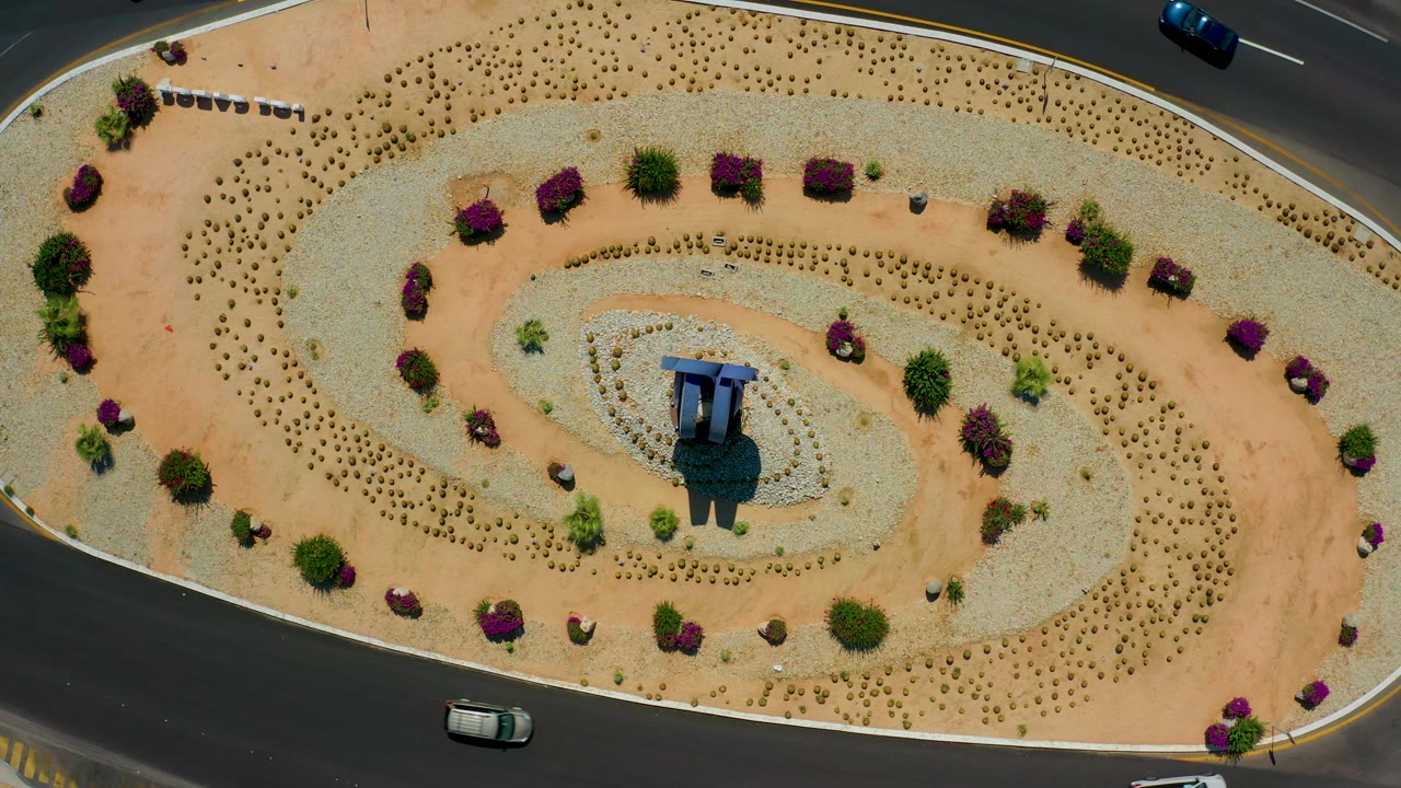 Aerial view of an oval landscaped traffic island with cars on nearby lanes.