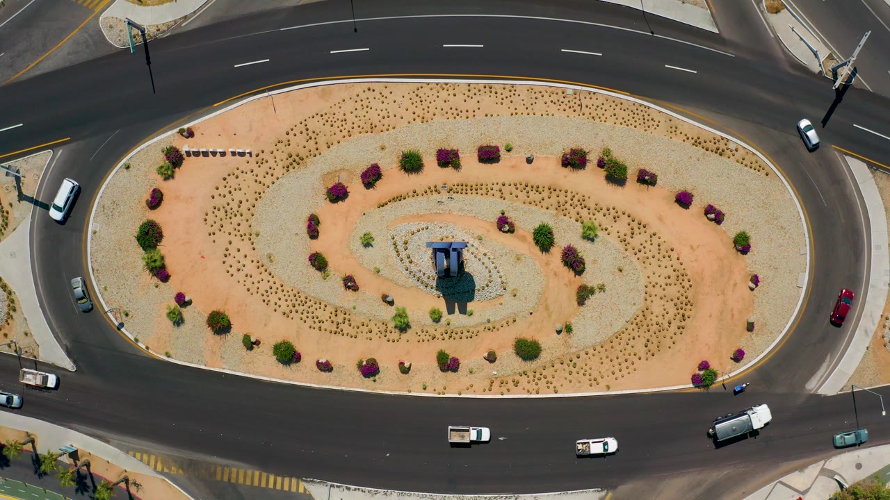 Top-down Los Cabos, Mexico road view with a central planted oval, cars on both sides of the roadway, and no visible people in the frame.