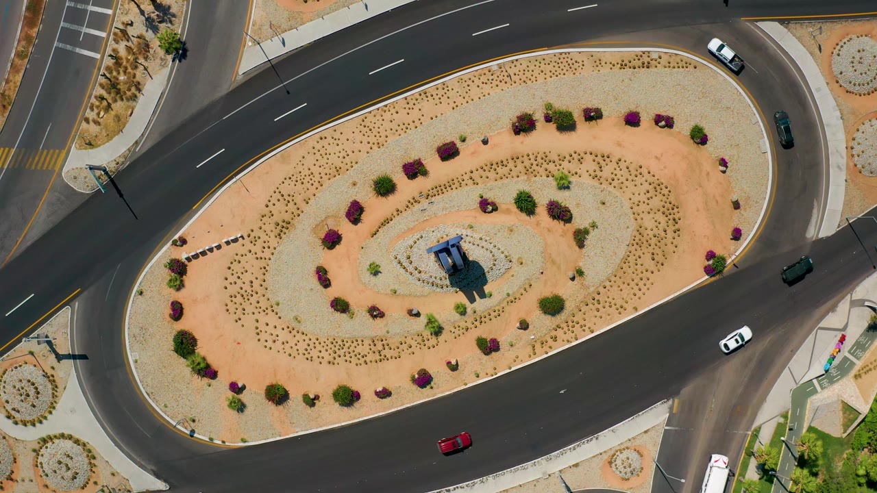 Cars spaced around a desert-planted traffic circle
