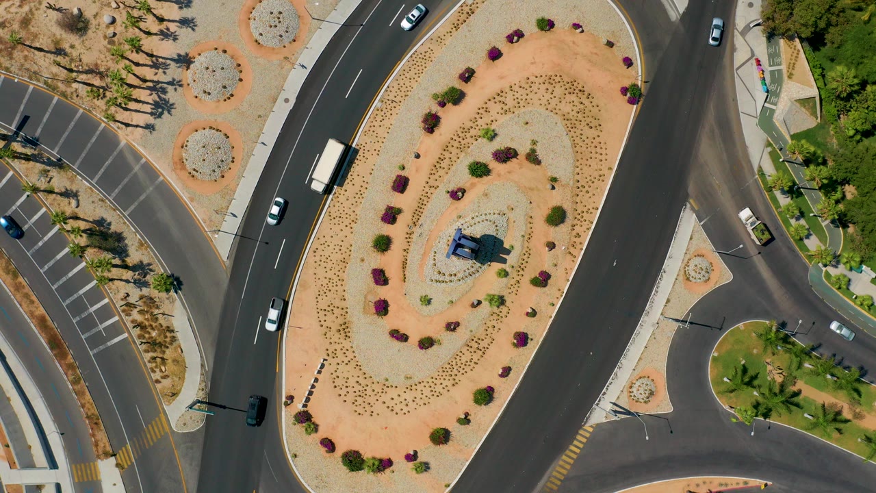 Overhead view of curved roads around a landscaped oval median with cars and a truck.