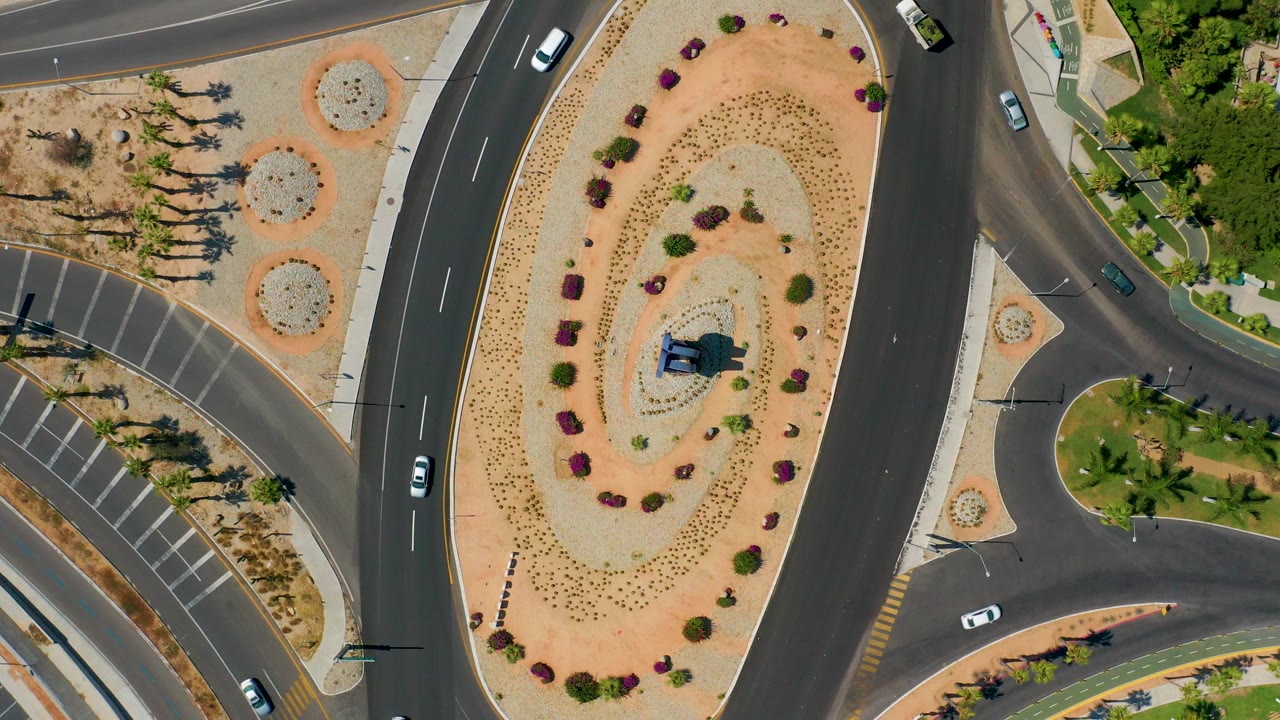 Overhead roads curve around a landscaped desert median with cars nearby.