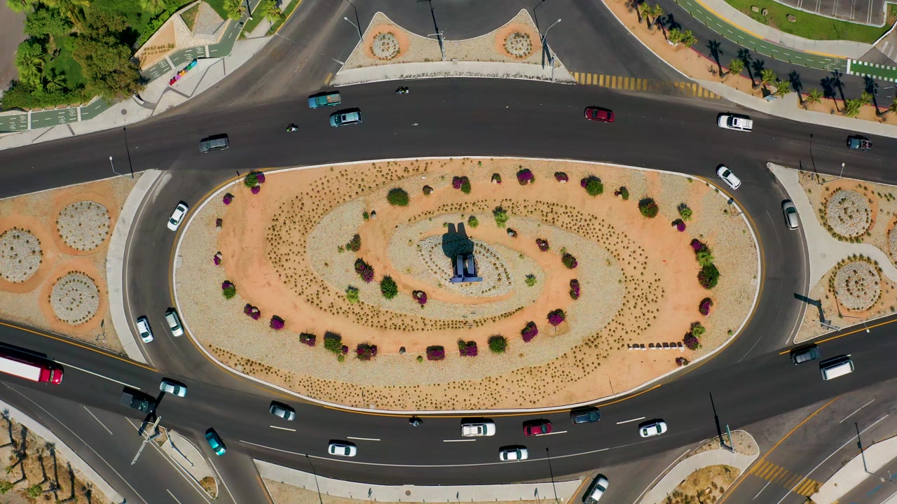 Overhead Los Cabos traffic circle with a red bus near the lower edge, small cars in several lanes, and no visible people.