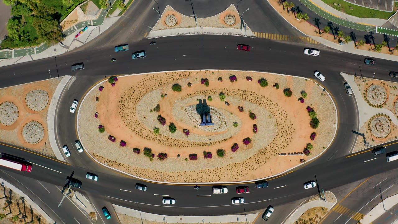 A Los Cabos roundabout seen from directly above, with vehicles spread across the upper and lower roads and no visible people.