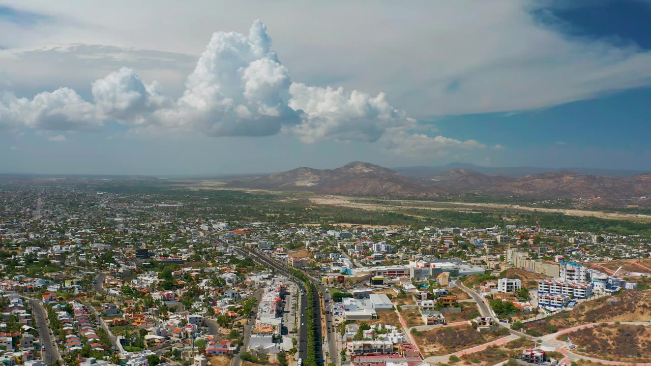Wide drone view of city blocks below clouds and hills