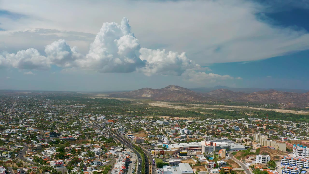 Wide aerial view of city blocks beneath tall white clouds