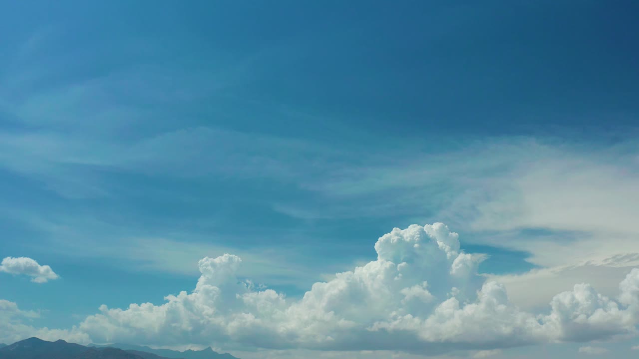 Los Cabos, Mexico frame with a broad blue sky, clustered white clouds centered over low mountain ridges, and no visible people.