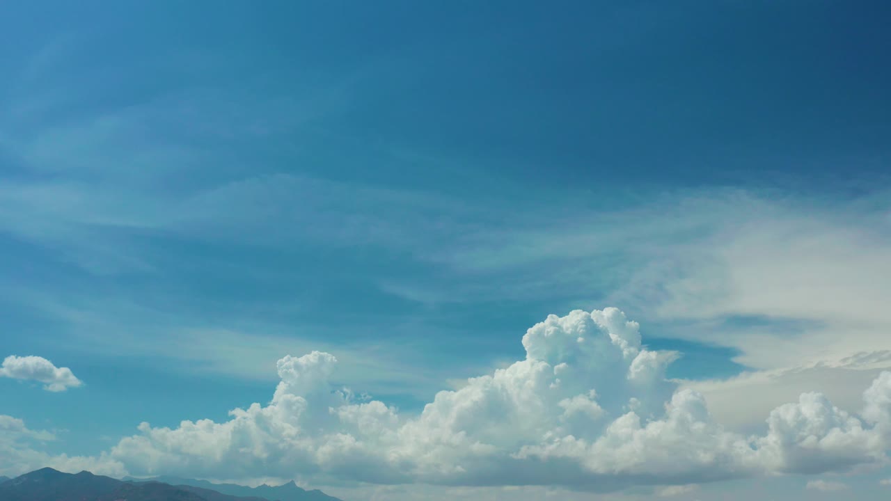 Los Cabos, Mexico view with layered blue sky, a tall cumulus cloud bank, faint mountain silhouettes along the bottom edge, and no visible people.