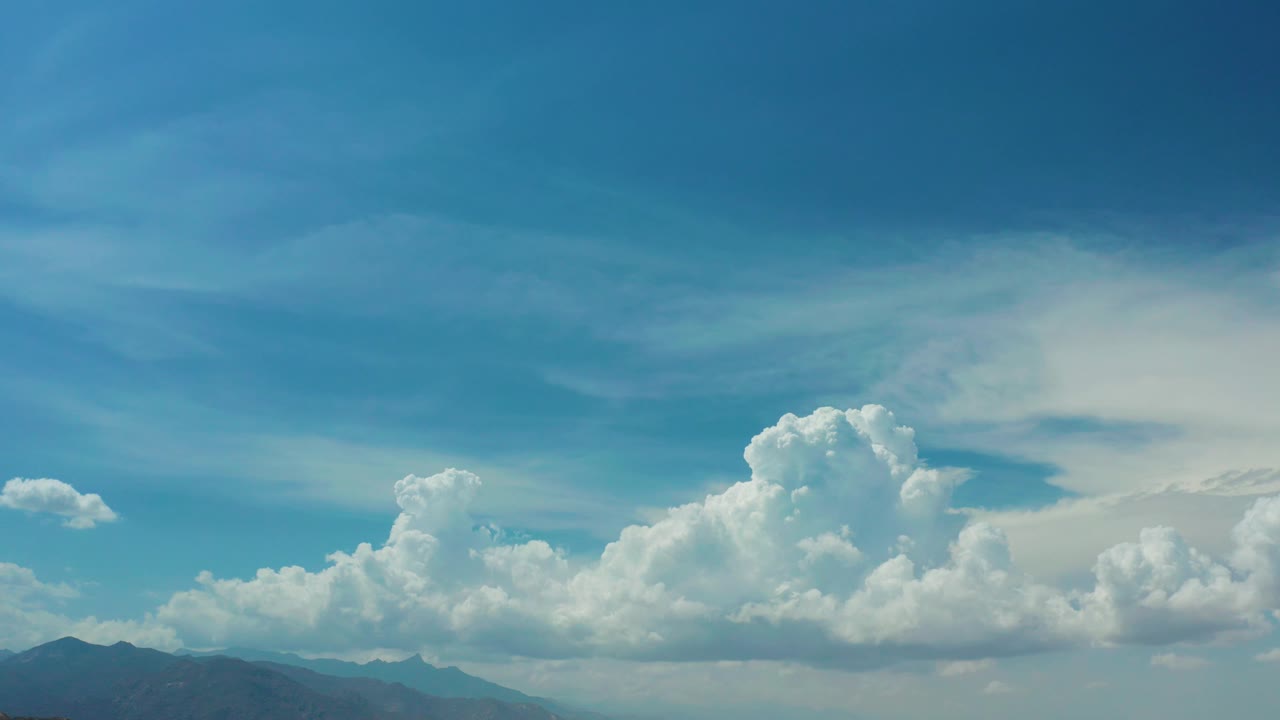 Los Cabos sky frame with the tallest white cloud mass right of center, darker mountain shapes along the bottom, and no visible people.