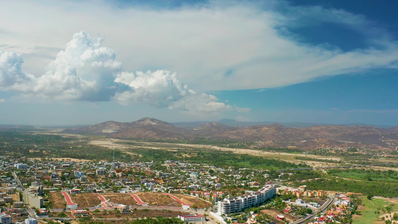High view across buildings, open land, hills, and clouds.