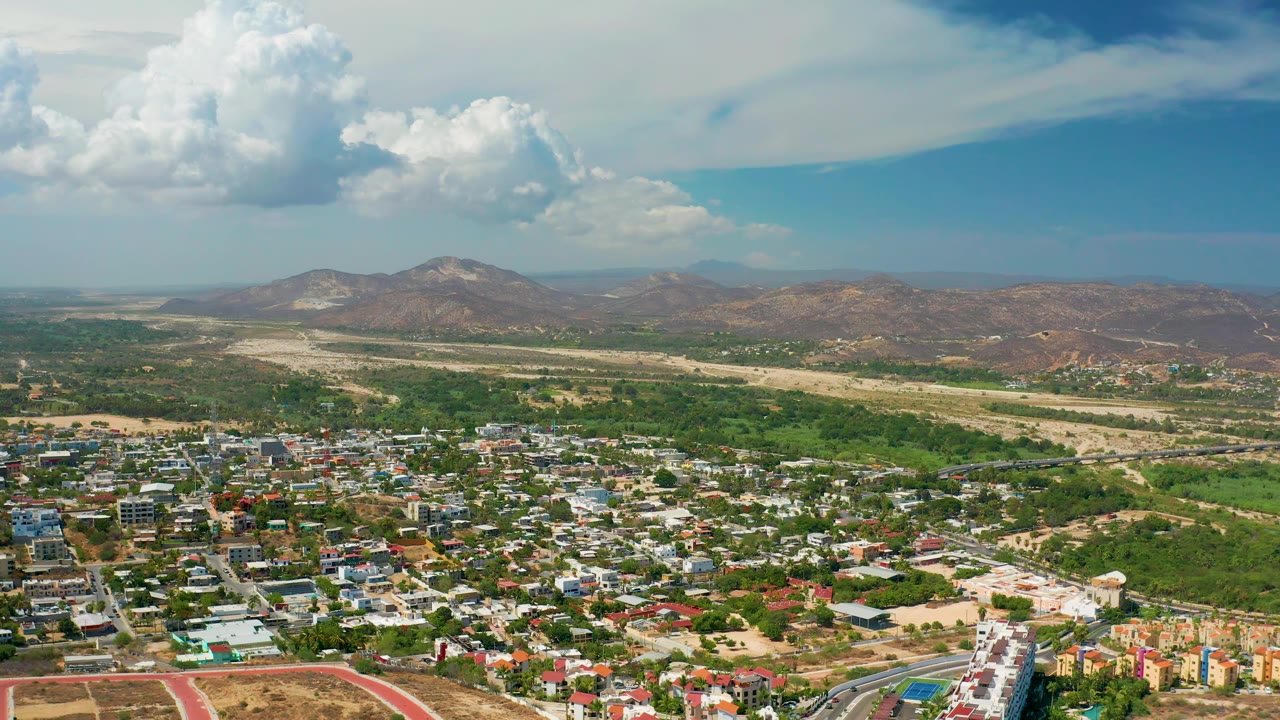 Town rooftops and roads spread below dry mountains under clouds.