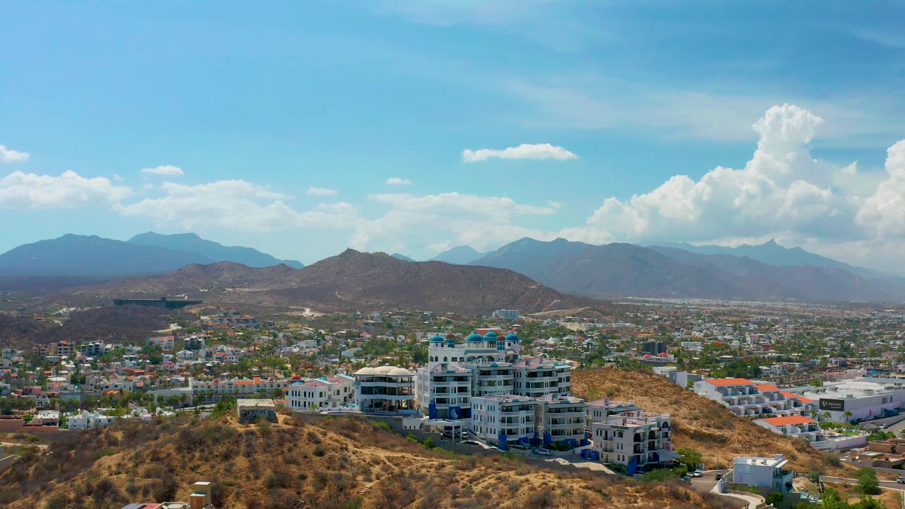 Hillside building complex overlooking city blocks and distant mountains under blue sky.