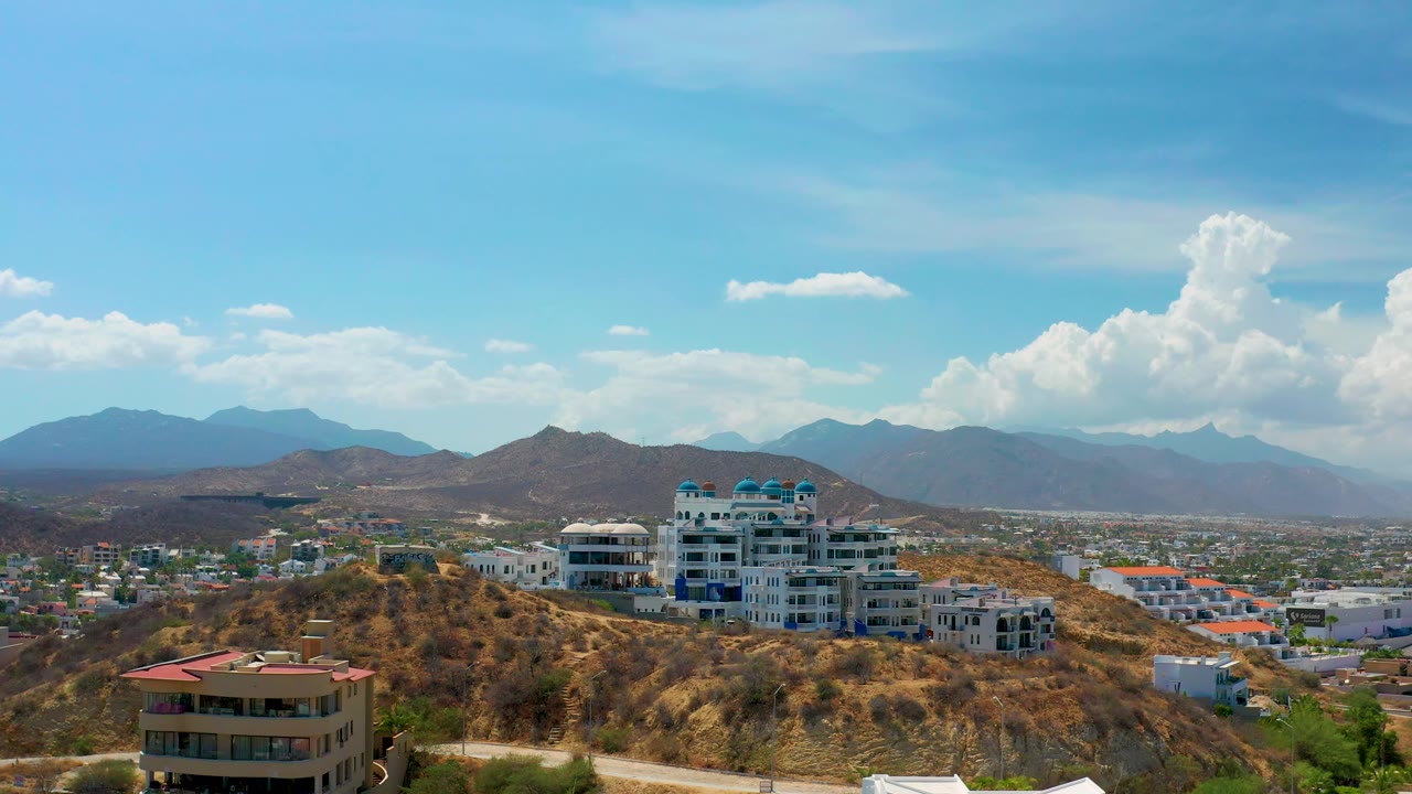 City and hillside buildings under bright sky with mountain backdrop.