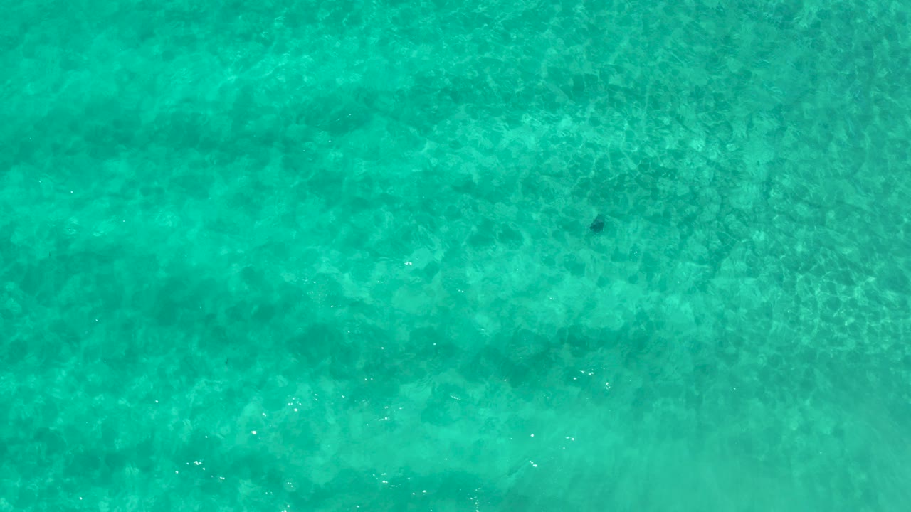Overhead view of turquoise water over the ocean floor in Los Cabos, Mexico, with faint ripples and no visible people.