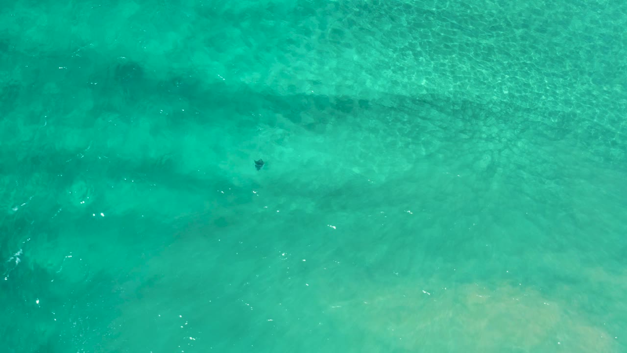 Aerial turquoise water with darker underwater streaks and ripples.
